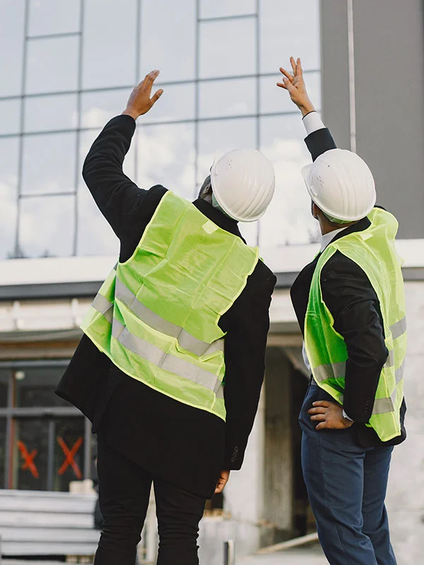 2 people with white hats and light green vests checking out a construction site